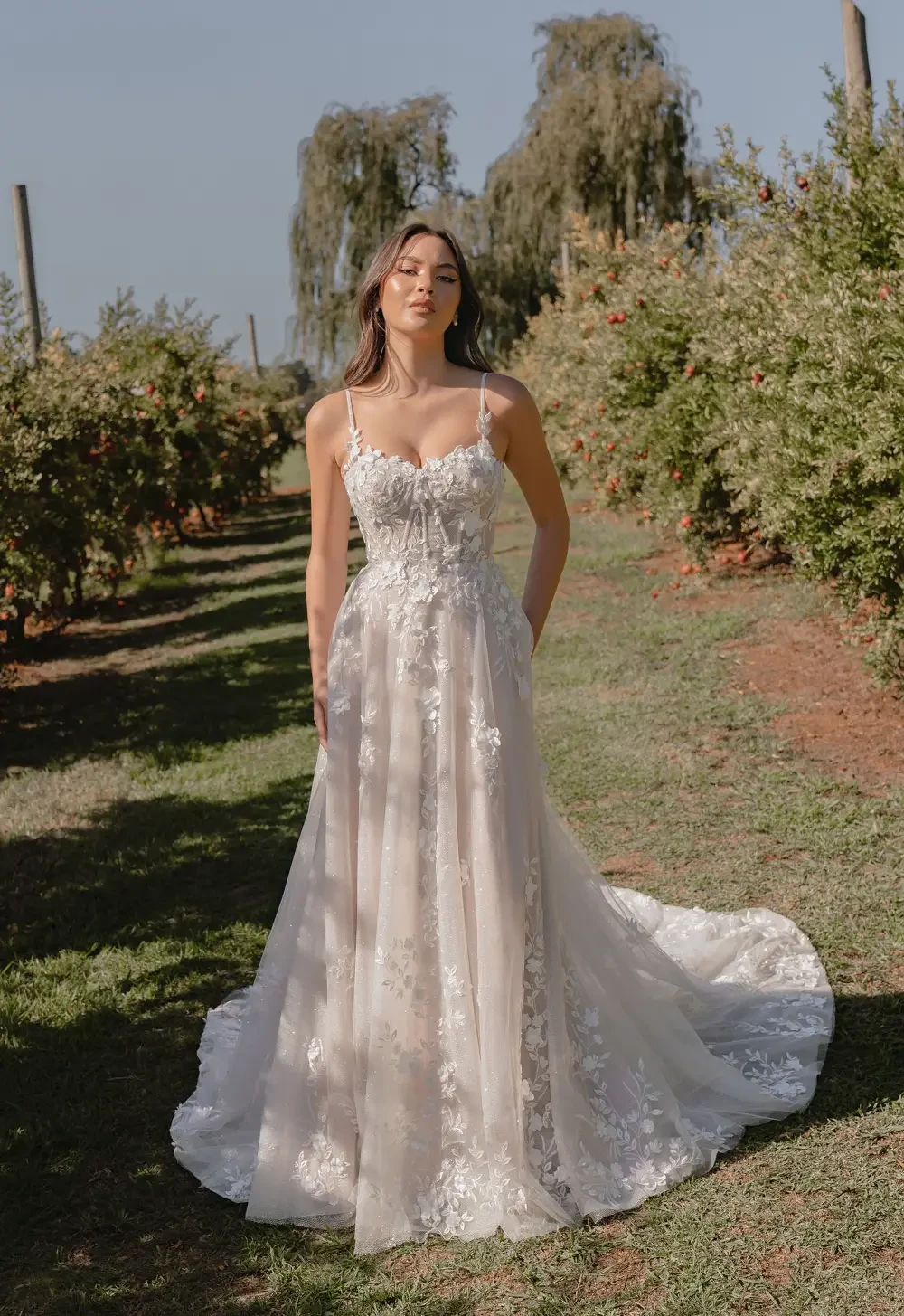 A woman in a beautiful, lace wedding gown stands in a lush garden setting.